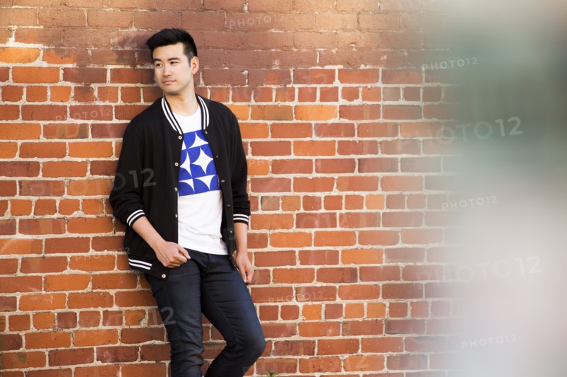 Smiling Chinese man leaning on red brick wall