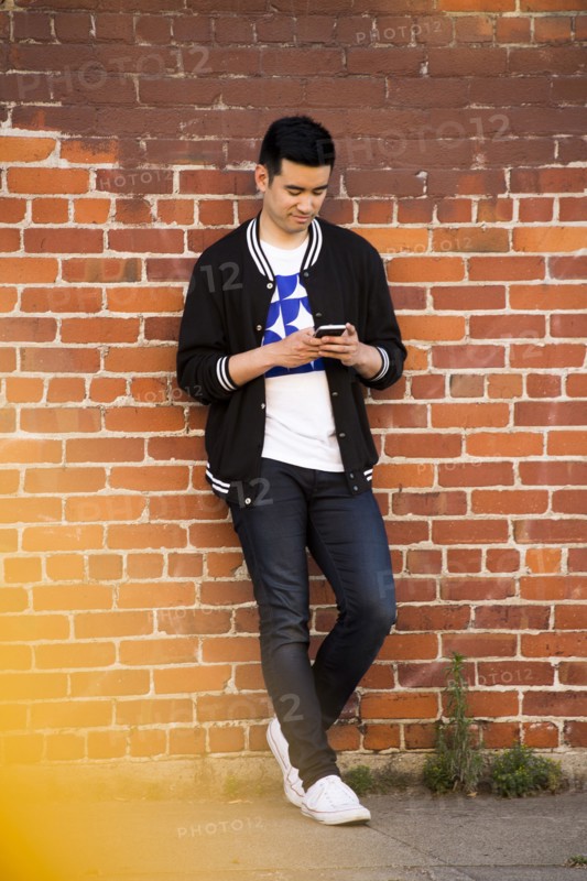 Chinese man leaning on brick wall texting on cell phone