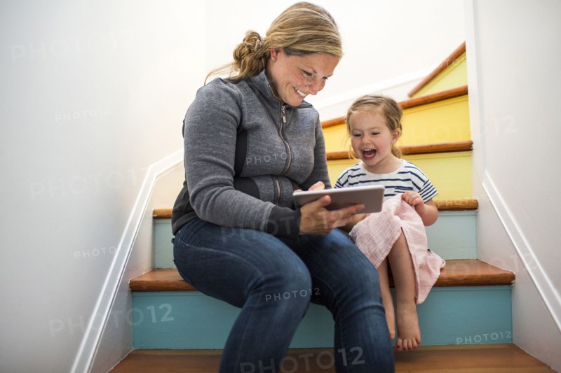 Caucasian mother and daughter using digital tablet on staircase