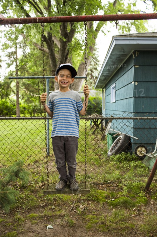 Smiling mixed race boy standing on backyard swing