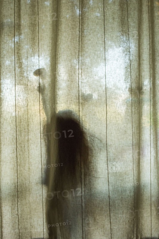 Silhouette of Caucasian girl touching heart-shape behind window curtain