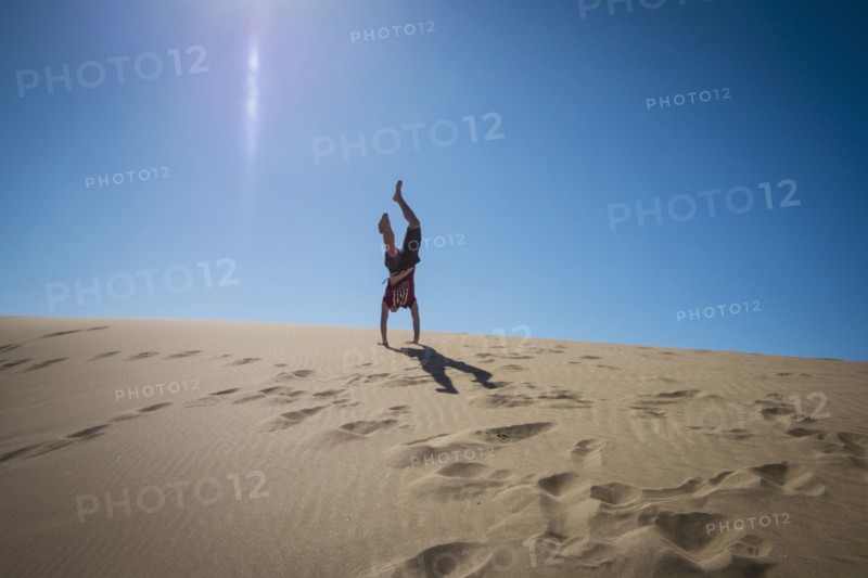 Caucasian teenage boy doing cartwheels on sand dune