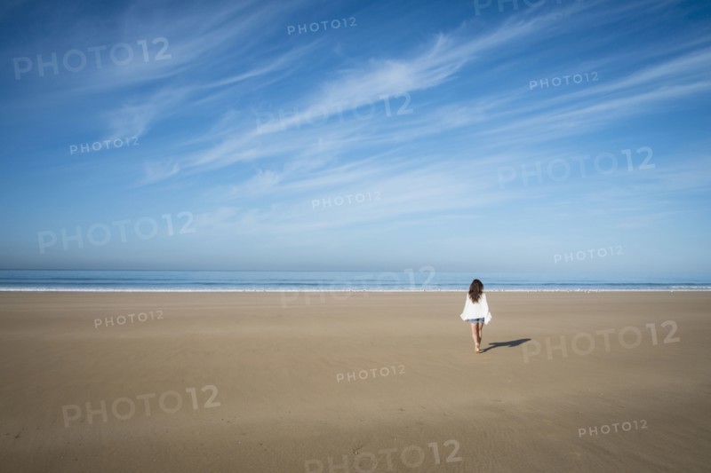 Caucasian woman walking on beach under blue sky