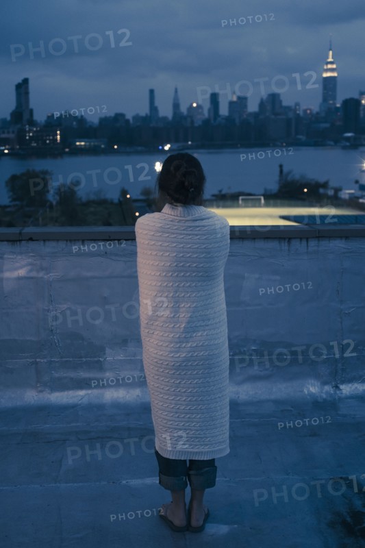 Caucasian woman wrapped in blanket admiring urban waterfront from rooftop