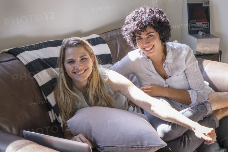 Caucasian lesbian couple smiling on sofa
