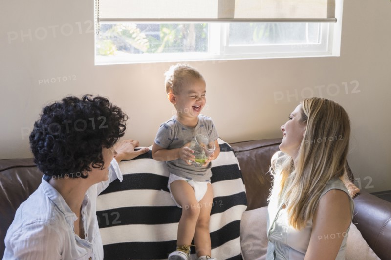 Caucasian lesbian mothers laughing with baby son on sofa
