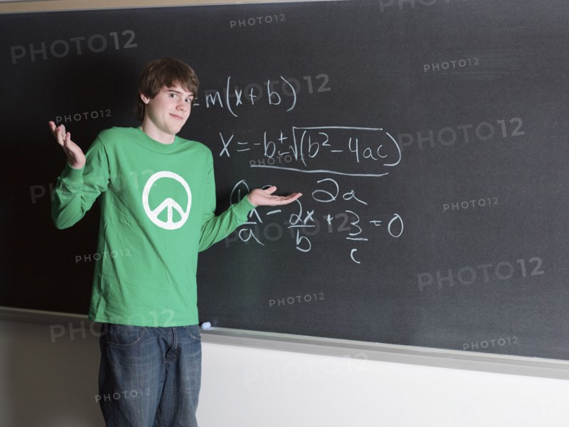 Student shrugging in confusion at chalkboard in classroom