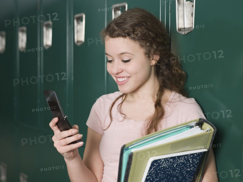 Mixed race student using cell phone by locker in school hallway