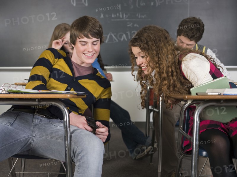 Students using cell phone at desk in classroom