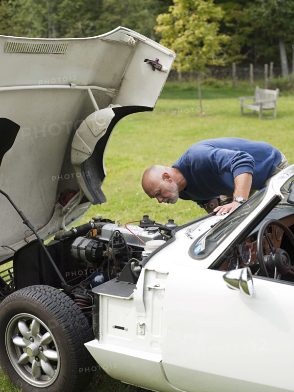 Older man examining broken-down convertible in park