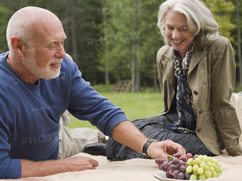 Older couple eating grapes at picnic in park