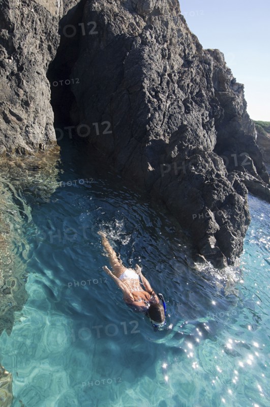 Woman swimming in ocean by rocky cliffs