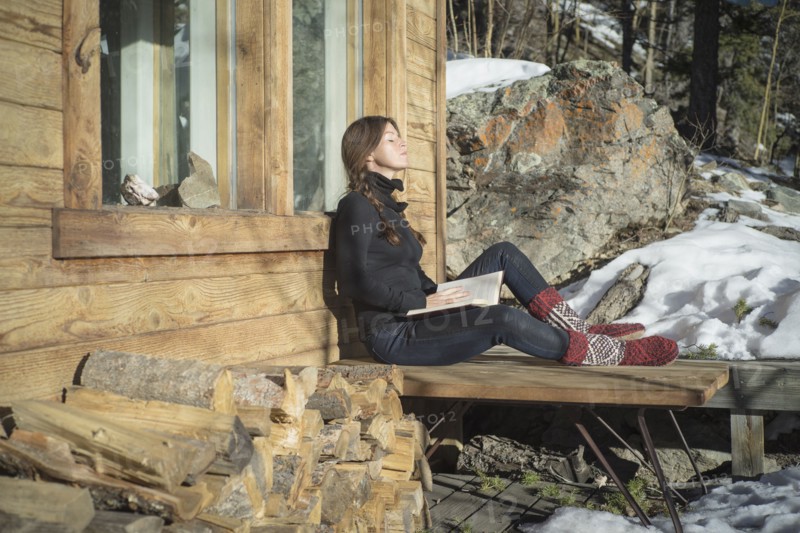 Caucasian woman reading book on cabin porch
