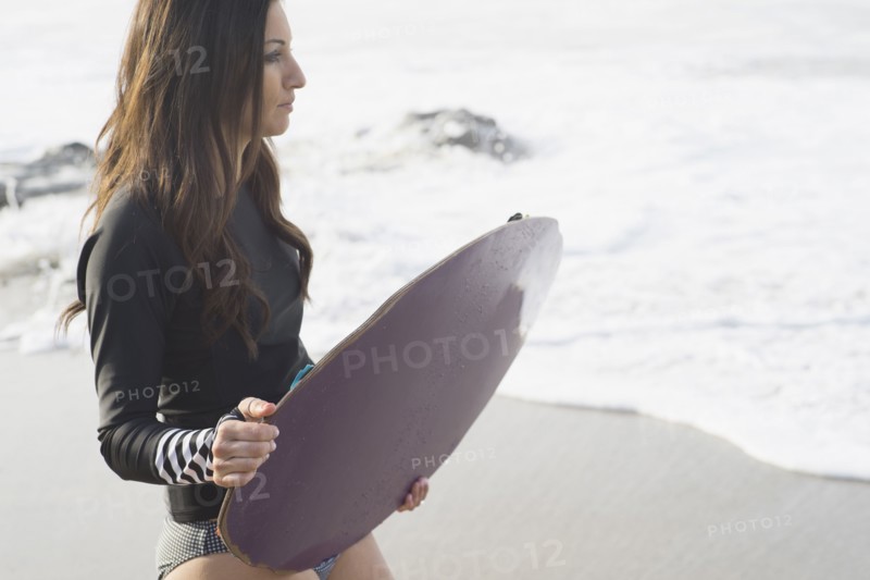 Caucasian woman holding skimboard at beach