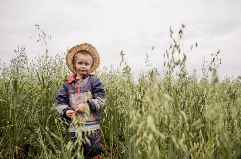Caucasian boy standing in tall grass in rural field