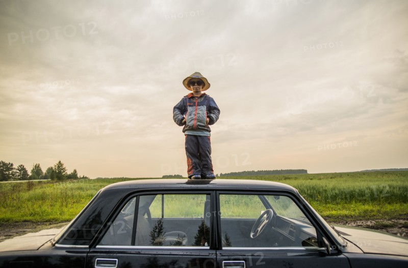 Caucasian boy standing on car roof in rural field