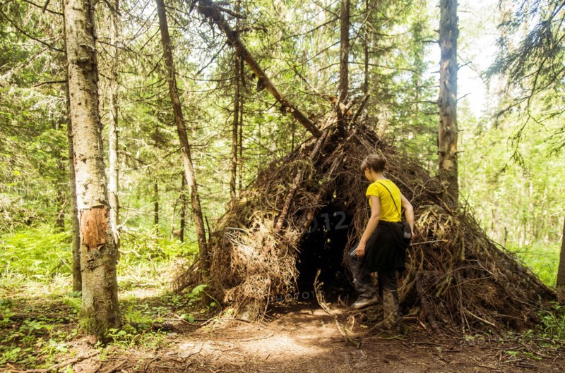 Caucasian boy playing in thatched teepee fort in forest