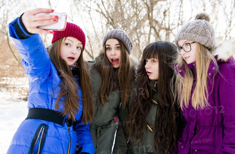 Caucasian girls taking cell phone photograph in snowy field