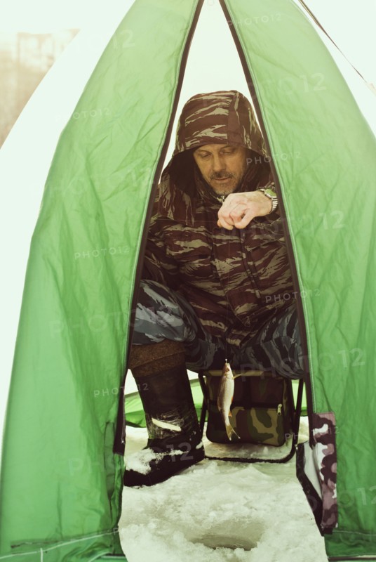 Caucasian hiker ice fishing in tent