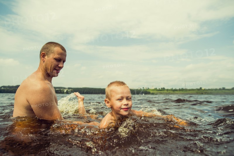 Caucasian father and son swimming in lake