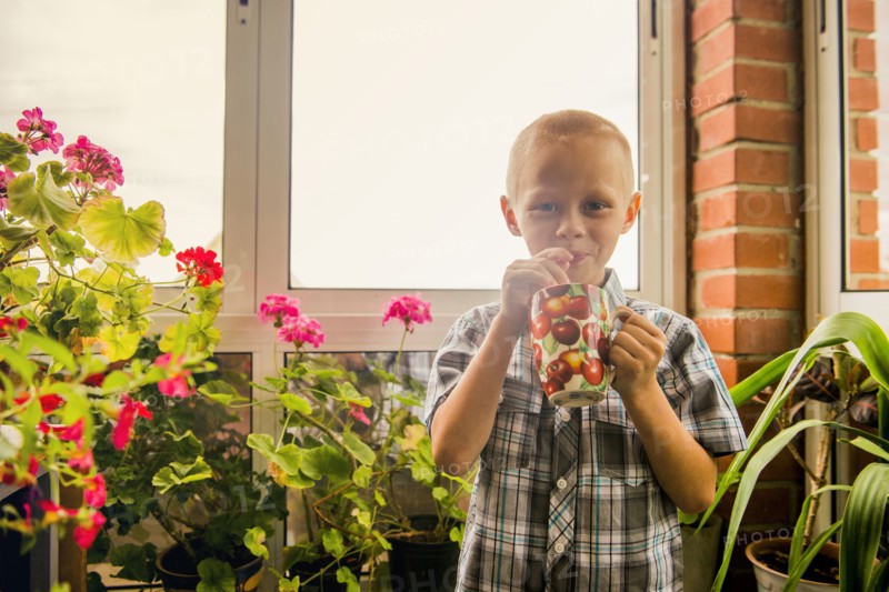 Caucasian boy drinking juice from mug by window
