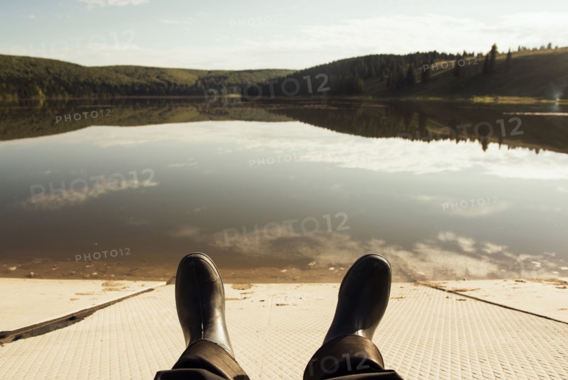 Boots of person resting on dock at lake