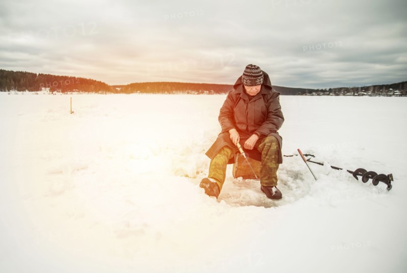 Man ice fishing in frozen lake