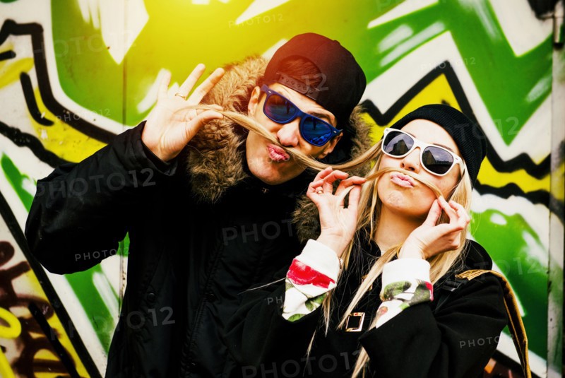 Couple making mustache with hair of woman at graffiti wall