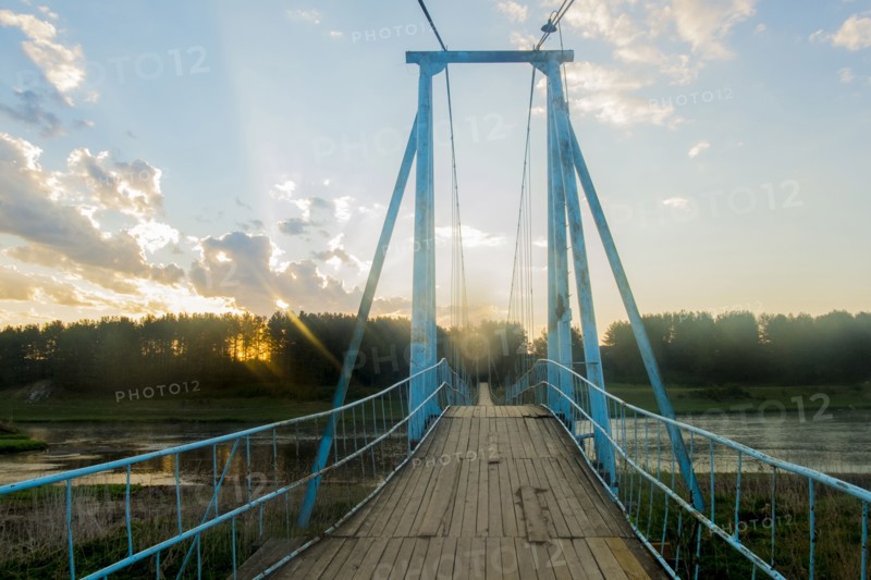 Sunbeams on wooden footbridge over river