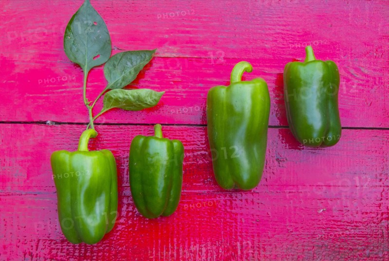 Close up of row of green peppers on red wooden table