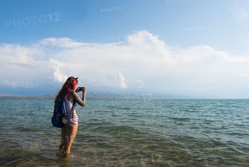 Caucasian woman wading in ocean photographing with cell phone