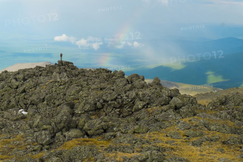Man standing on rock formation looking at rainbow