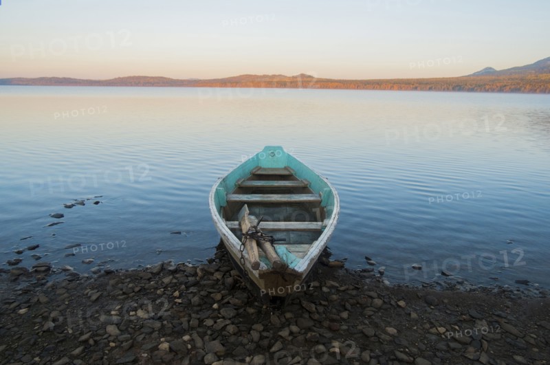 Empty rowboat on rocky shore of lake at sunset