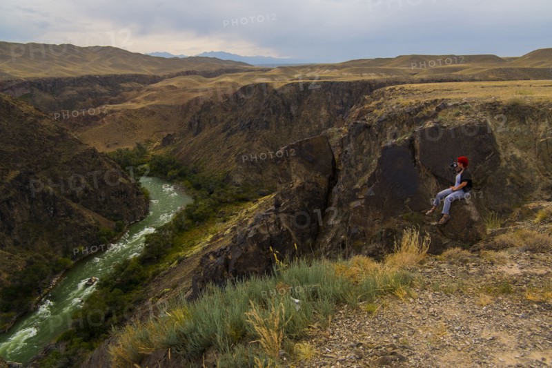 Caucasian woman sitting on mountain rocks photographing river