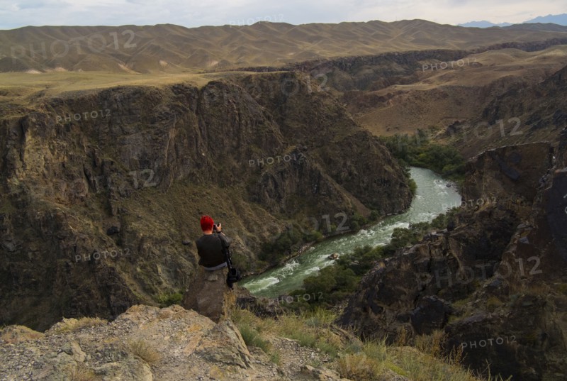 Caucasian woman sitting on mountain rocks photographing river
