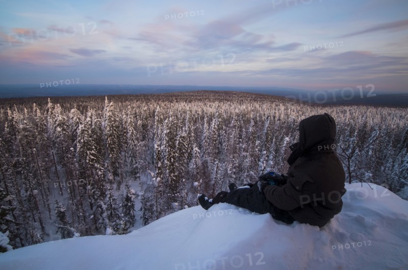 Caucasian man sitting in snow admiring scenic view of forest