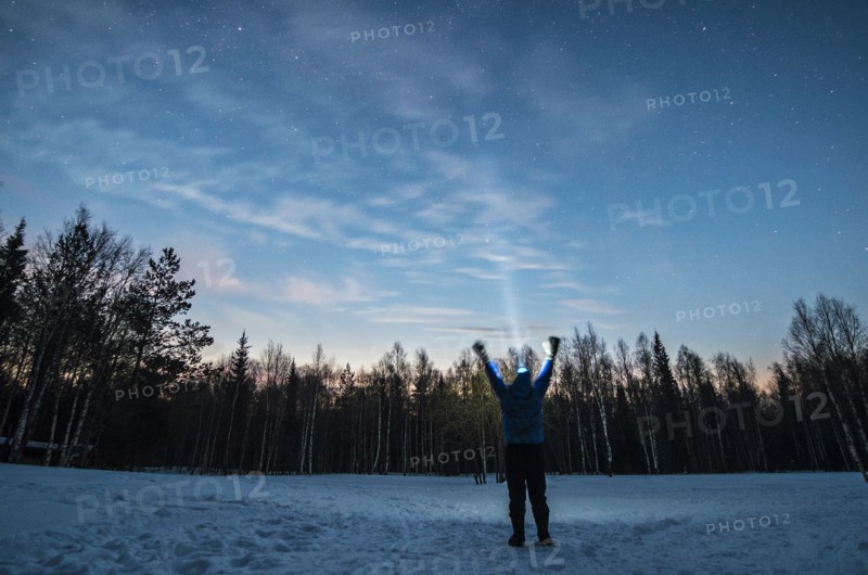 Caucasian man wearing headlamp with arms raised in winter