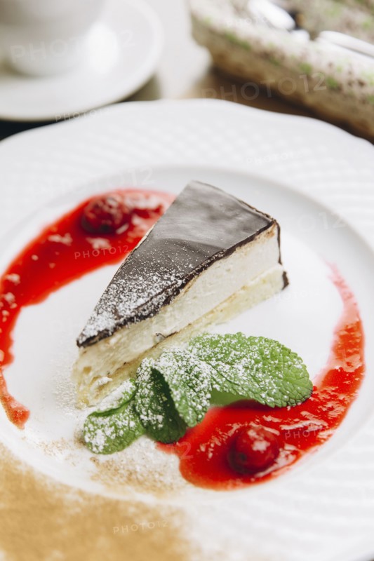 Cheesecake slice on plate with powdered sugar and berry sauce