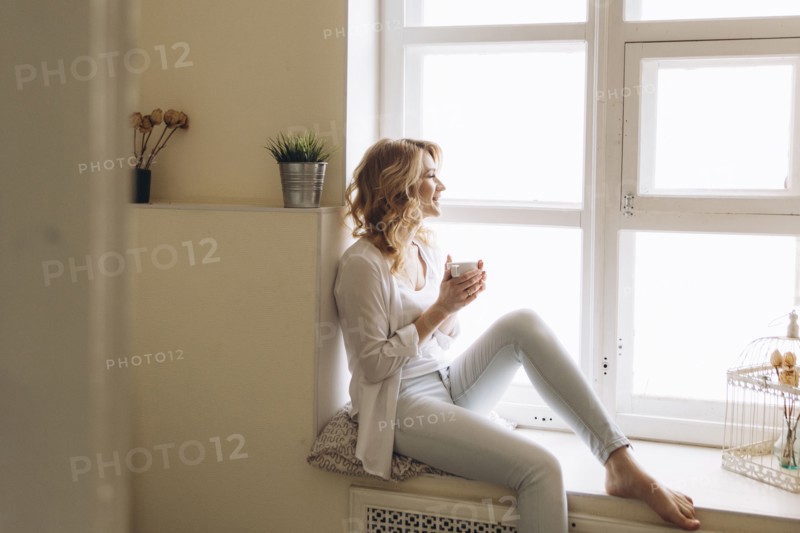 Middle Eastern woman sitting in window sill drinking coffee