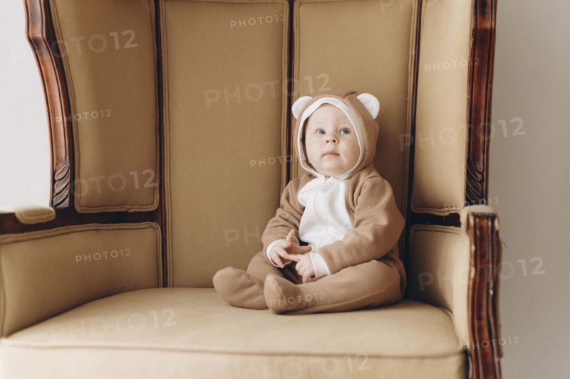 Caucasian baby boy sitting in armchair wearing bear costume