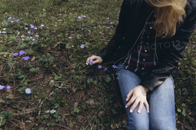 Woman sitting in grass picking purple flower