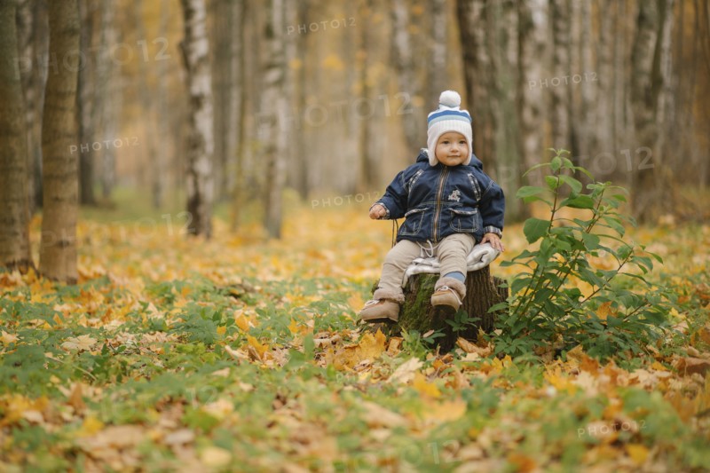 Middle Eastern baby boy sitting on tree stump in autumn
