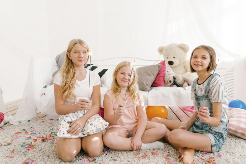 Portrait of smiling Middle Eastern sisters holding sparklers in bedroom