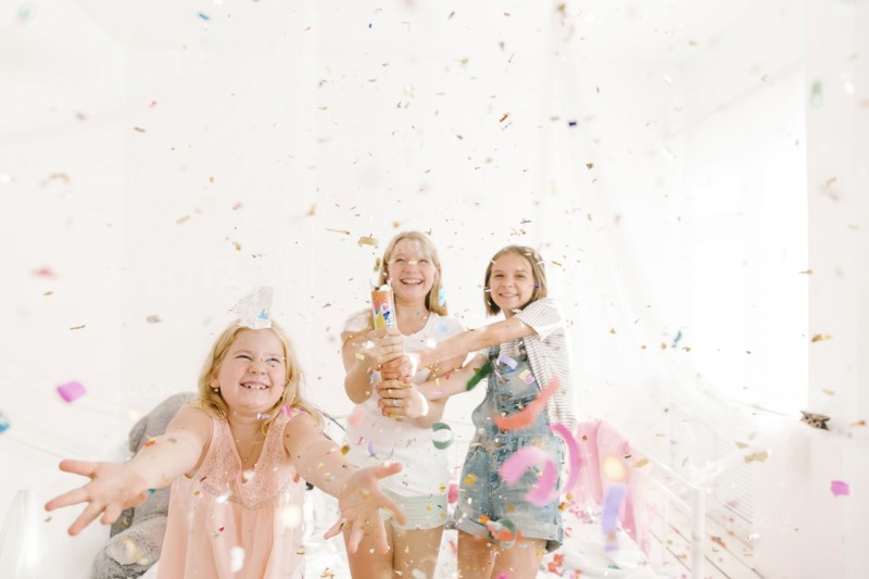 Smiling Middle Eastern girls throwing confetti in bedroom