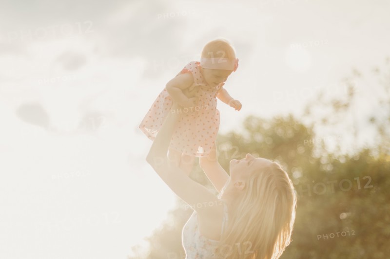 Mother lifting baby daughter on sunny day