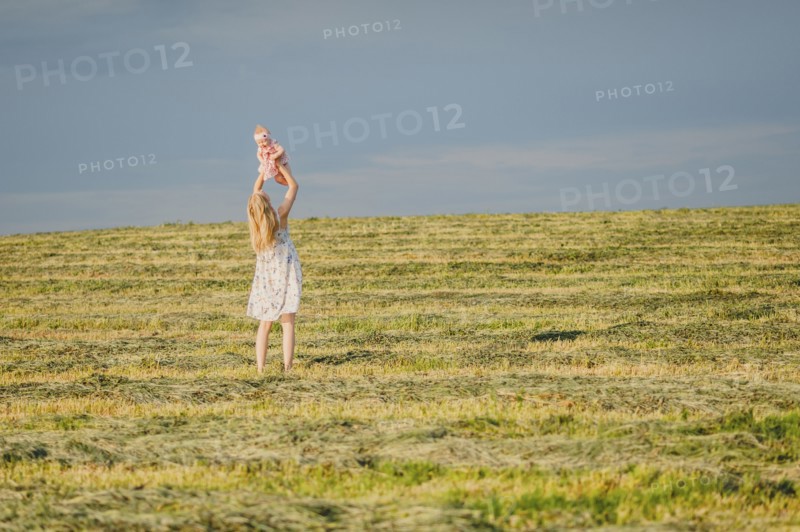 Mother lifting baby daughter in field