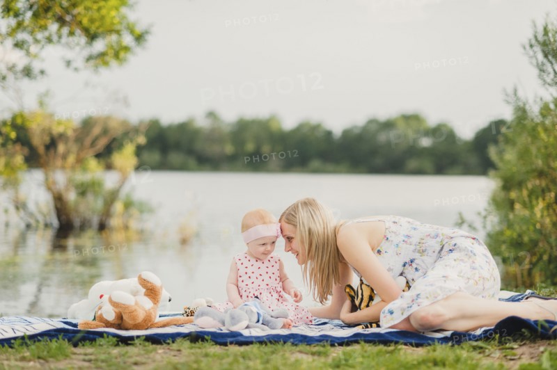 Mother and daughter playing with stuffed animals on blanket near lake