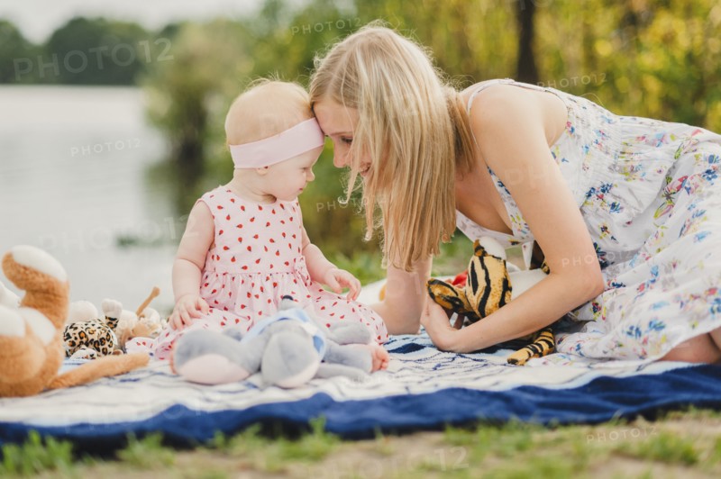 Mother and daughter playing with stuffed animals on blanket near lake