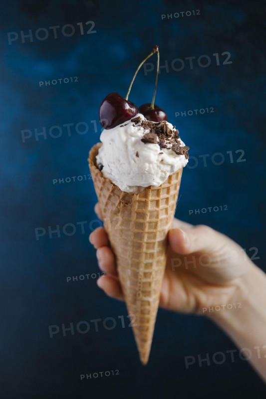 Hand holding ice cream cone with cherries