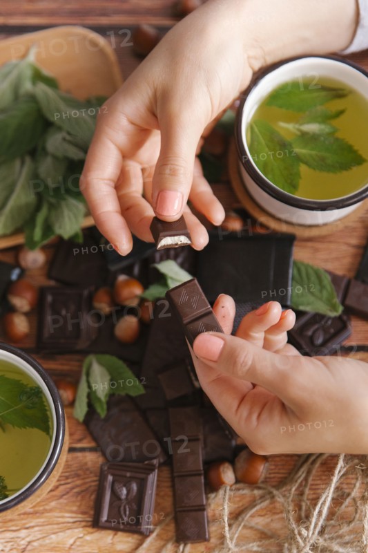 Hands of woman breaking chocolate near green tea